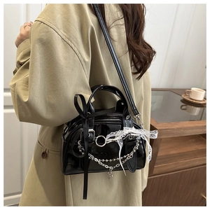 Detail of black glossy leather crossbody bag with silver chains and white lace trim