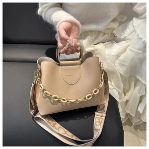 Detail view of beige bucket bag with metal U-handle, chain, and wide woven strap