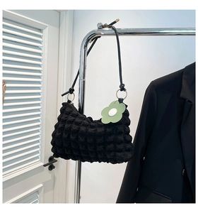 Detail of black bubbly textured shoulder bag with a pale green floral charm hanging