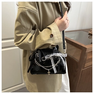 Detail of black patent leather crossbody bag with silver chains and lace bow