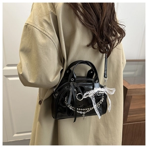 Detail of glossy black patent leather bag with silver chains and white lace bow