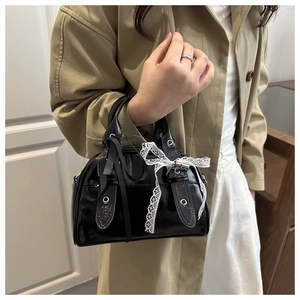 Detail of black patent leather bag with lace bow and silver metal hardware accents