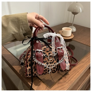 Detail of leopard print crossbody bag with red trim, lace bows, and silver chain