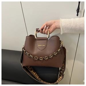 Detail of dark brown bucket bag featuring gold lettering and printed wide strap