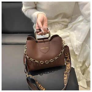 Detail of dark brown bucket bag featuring gold handle and fashion-patterned fabric strap