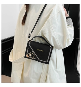 Detail of black crossbody bag with white stitching and gold metal lock on a trench coat