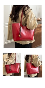 Detail of red oil wax leather tote bag featuring a woven knot and golden bead pendant