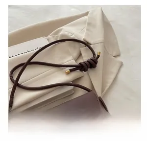 Detail of dark brown leather crossbody bag with knot strap and gold metal clasp