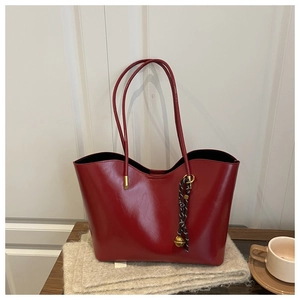 Detail of deep red oil wax leather tote bag with woven bell charm on a knit surface