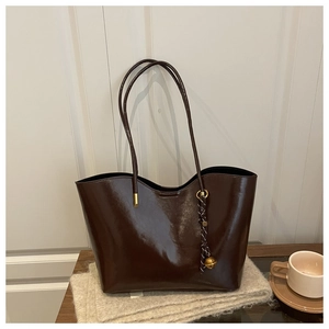 Detail of dark brown oil-wax leather tote with woven charm on soft plush background
