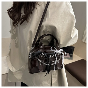 Detail of dark brown patent leather crossbody bag with chain and lace bows