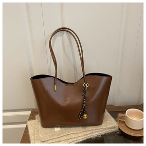 Detail of dark brown faux leather tote bag with stylish braided bell pendant on scarf