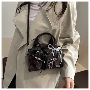Detail of dark brown patent leather bowling bag with chains, lace bows, and cross charm