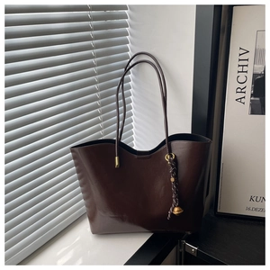 Detail view of large dark brown tote bag with woven pendant and gold hardware accents