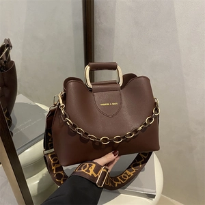 Brown bucket handbag with gold U-shaped handle and printed wide shoulder strap