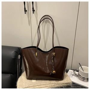 Detail of deep brown oil wax leather tote bag with metallic accents and woven pendant