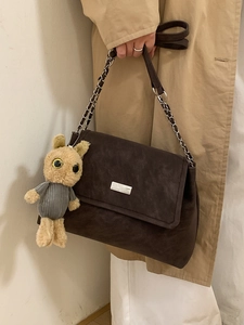 Braune Schultertasche mit Kette und Plüschtier-Anhänger auf einem Khaki-Mantel