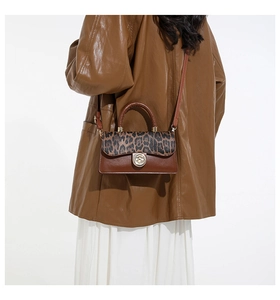 Detail of leopard print flap and gold twist lock on brown faux leather crossbody bag