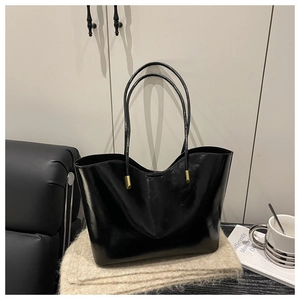 Detail of black oil-wax leather tote bag with glossy finish and gold metal accents