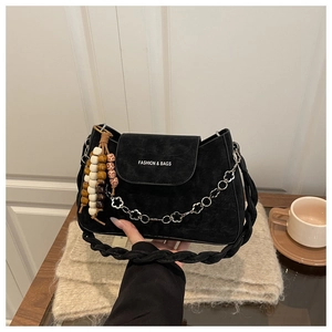 Détail du sac en daim noir avec chaîne vintage, bandoulière tissée et pompon perlé