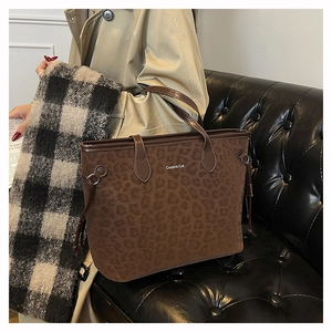 Détail du sac cabas léopard avec texte Creative Cat porté par mannequin sur canapé cuir