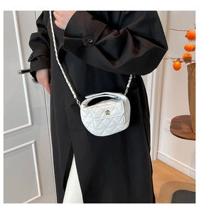 Detail van witte gewatteerde mini-crossbodytas met gouden bloemgesp op zwarte jas