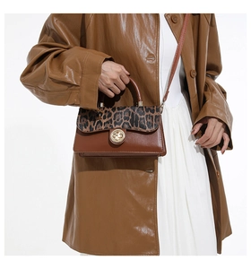 Detail of a chic leopard print crossbody bag with a round metal lock on a model