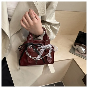 Detail of burgundy patent leather bag with silver chain, lace trim, and black bow accents