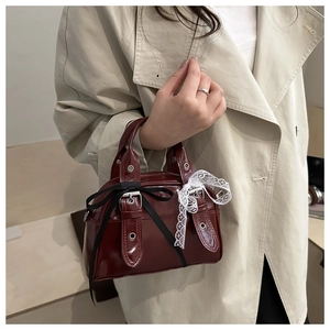 Detail of burgundy patent leather bag with black satin bow and white lace trim