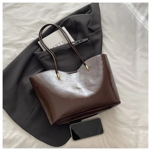 Detail of deep brown glossy tote bag featuring premium gold metal hardware and minimalist design