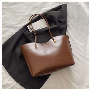 Brown oil wax leather tote bag shown on a white fabric background with elegant props