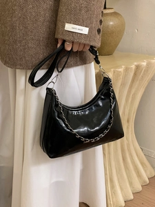 Sac hobo noir brillant avec chaîne argentée porté par un mannequin en tenue d'hiver
