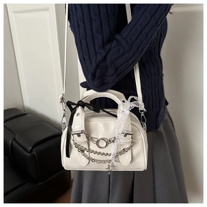 Close-up of white leather handbag with silver chains, cross pendant and lace bow details