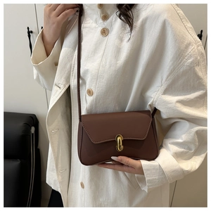 Close-up of a dark brown crossbody bag with a golden oval rotating lock on white shirt