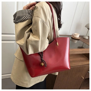 Detail view of large red oil wax leather tote bag with bell pendant on beige trench coat