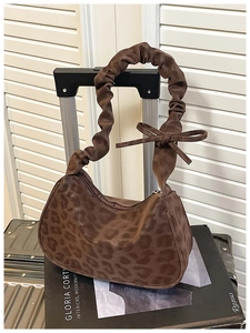 Close-up of leopard print bag with ruched strap and bow on a silver suitcase handle