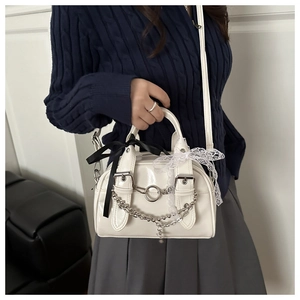 Detail view of white glossy Boston bag with chain, metal rings and lace bow charms