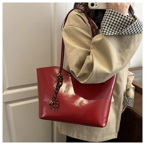 Glossy red faux leather tote bag detail with woven cord knot and gold bell charm
