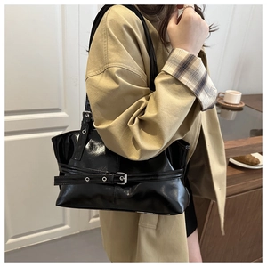 Side view of a glossy black leather tote bag with silver buckle details on a female model