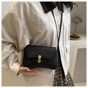 Close-up of black matte flap bag with gold oval metal buckle held by a model