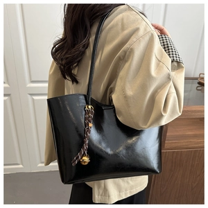 Detail of glossy black oil wax leather tote bag with decorative woven bell pendant