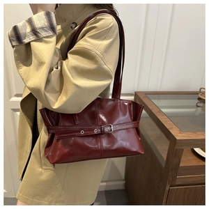 Detail of dark red glossy shoulder bag with vintage buckle strap on a model