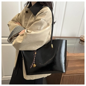 Detail of a large black oil wax leather tote bag with woven charm on beige trench coat