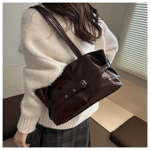 Detail of a dark brown patent leather shoulder bag with a silver buckle strap design