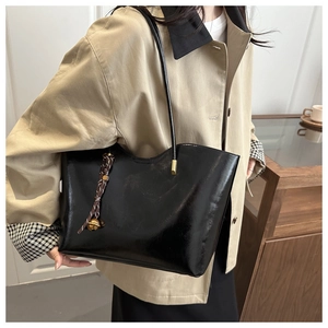 Detail of black glossy leather tote bag showing wavy top edge and golden hardware
