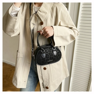 Close-up of matte black leopard print handbag with Creative Cat logo on beige coat