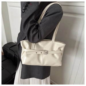 Detail view of cream white leather shoulder bag with buckle strap on a grey suit model