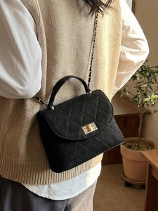 Quilted black suede crossbody bag with gold chain strap worn by a model in a cozy room