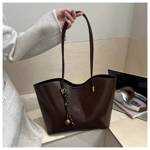 Detail of deep brown oil wax leather tote bag with a golden bell pendant and rope charm