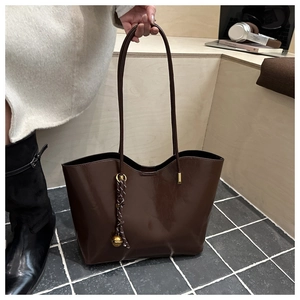Detailed view of deep brown oily leather tote bag with braided knot and bell charm detail